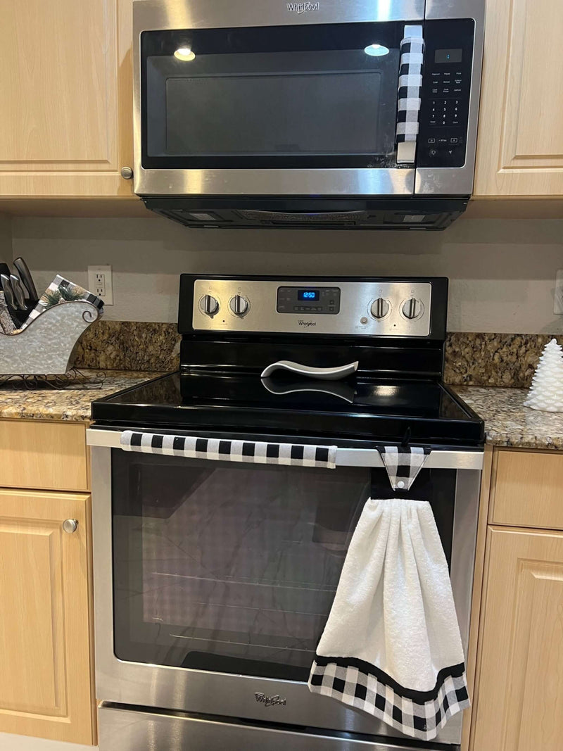 Stainless steel oven with a checkered towel hanging on the handle in a kitchen setting, and handle covers to match.