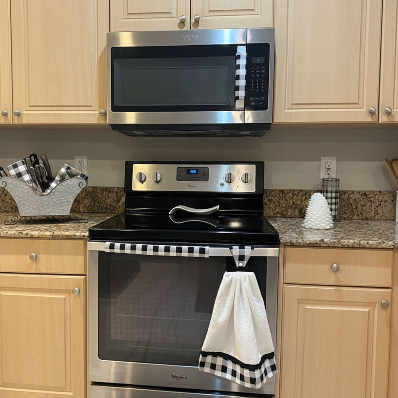 Stainless steel oven with a checkered towel hanging on the handle in a kitchen setting, and handle covers to match.