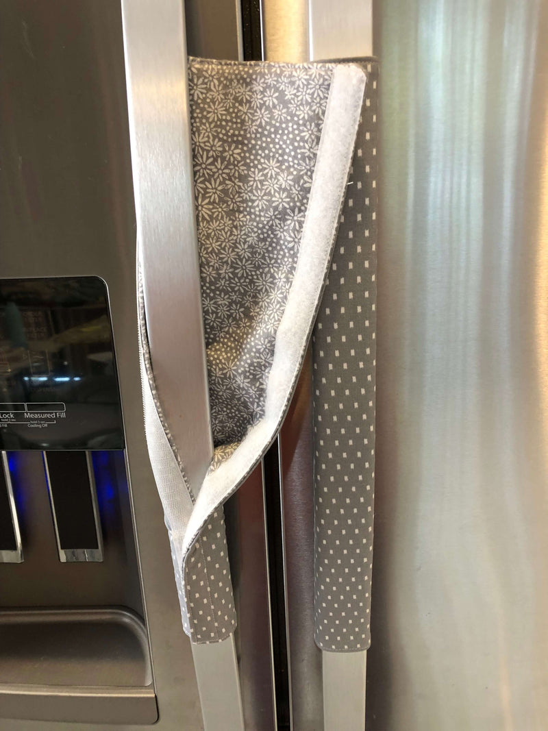 Grey and white gerbera daisy handle covers for kitchen appliances on a refrigerator door.