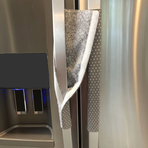 Grey and white gerbera daisy handle covers for kitchen appliances on a refrigerator door.