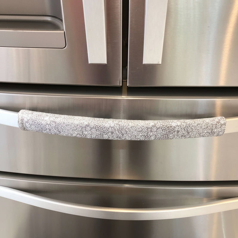 Grey and white gerbera daisy handle covers on stainless steel refrigerator door handle.