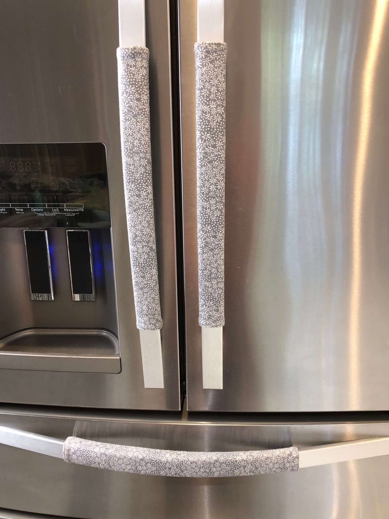 Grey and white gerbera daisy handle covers on stainless steel refrigerator handles.