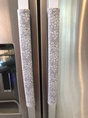 Grey and white gerbera daisy handle covers for kitchen appliances on stainless steel refrigerator handles.