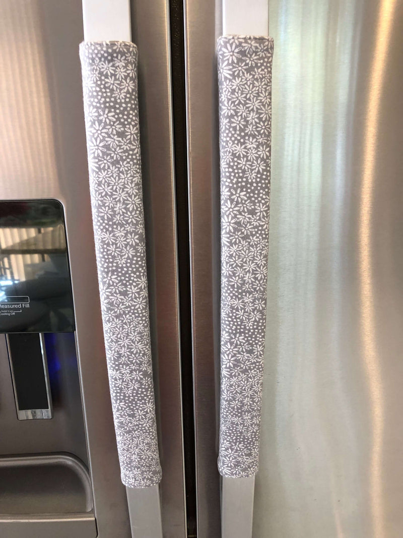 Grey and white gerbera daisy handle covers for kitchen appliances on stainless steel refrigerator handles.