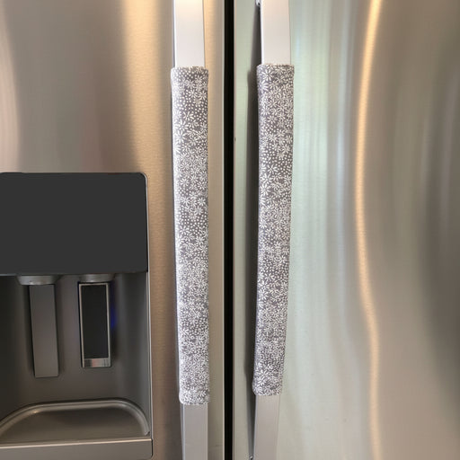 Grey and white gerbera daisy handle covers for kitchen appliances on stainless steel refrigerator handles.