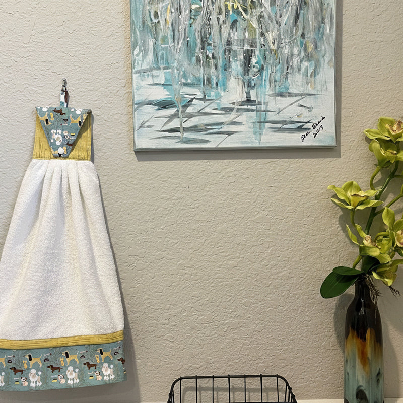 Handmade cute puppy print kitchen hand towel hanging next to modern wall art and decorative flowers.