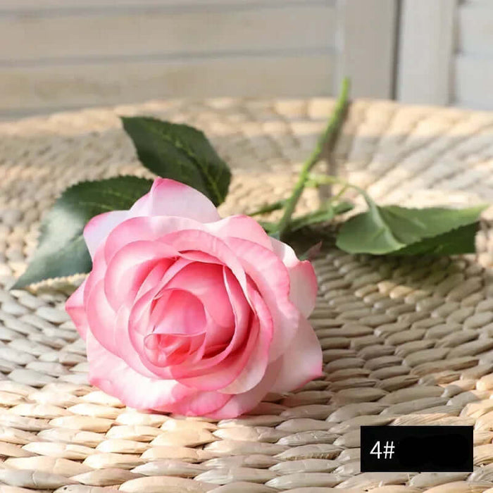 Latex real-touch artificial rose in soft pink hues resting on a woven surface, showcasing realistic details and vibrant colors.