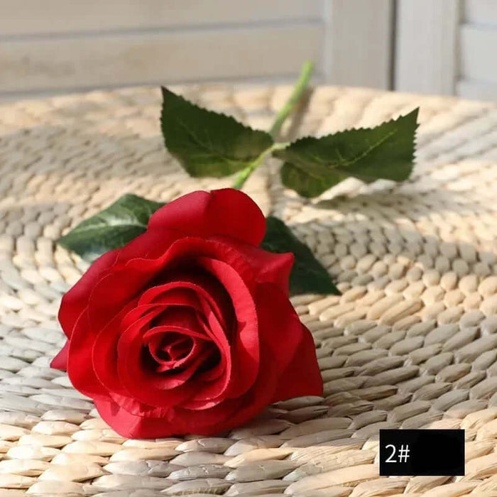 Latex real-touch artificial rose in full bloom on a woven surface, showcasing vibrant red petals and green leaves.