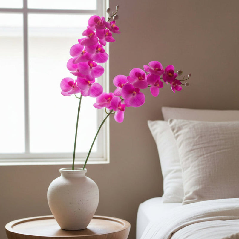 Fuchsia artificial butterfly orchid on a table beside a bed 