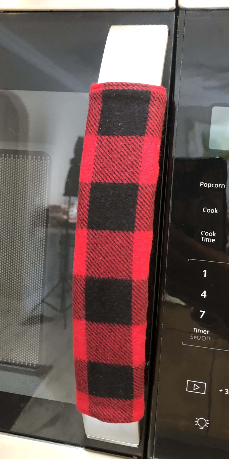 Red and black buffalo check appliance handle covers on a microwave, adding rustic charm to kitchen decor.