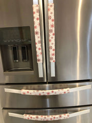Rose pink snowflake appliance handle covers on a stainless steel refrigerator, adding a festive touch to kitchen decor.