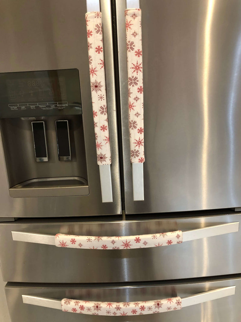 Rose pink snowflake appliance handle covers on a stainless steel refrigerator, adding a festive touch to kitchen decor.