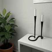 Black candle holder with two white candles on a white surface against a gray wall.