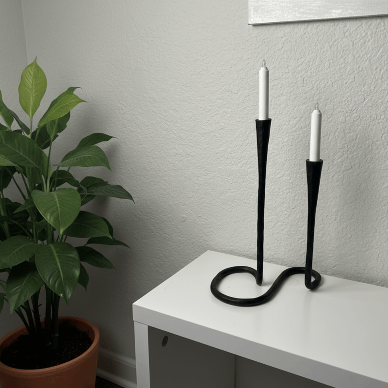 Black candle holder with two white candles on a white surface against a gray wall.