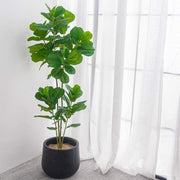Large realistic artificial ficus tree adding greenery to a modern home setting with sheer curtains.