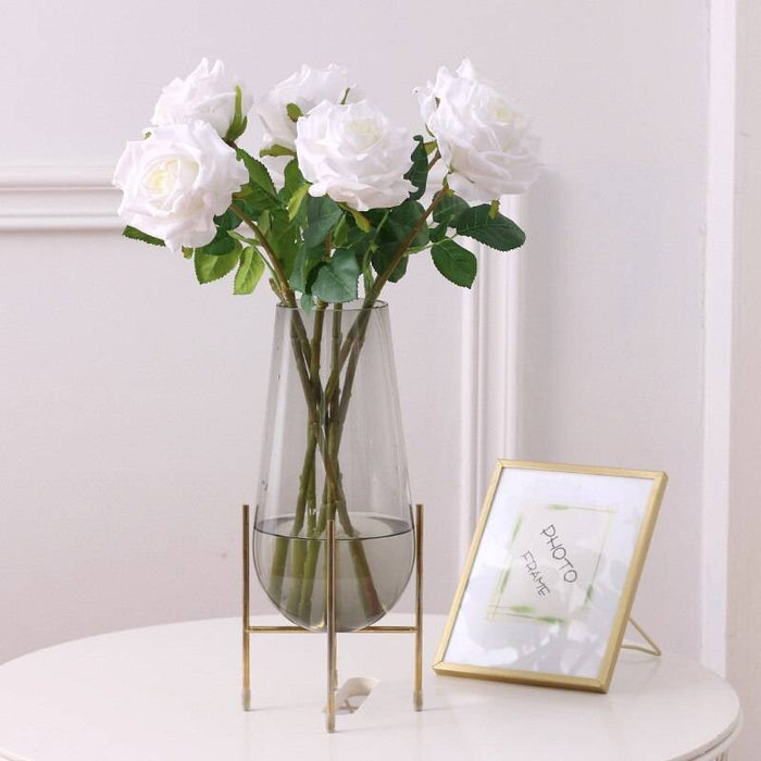 Realistic artificial rose stem in a clear vase with greenery enhancing home decor elegance.